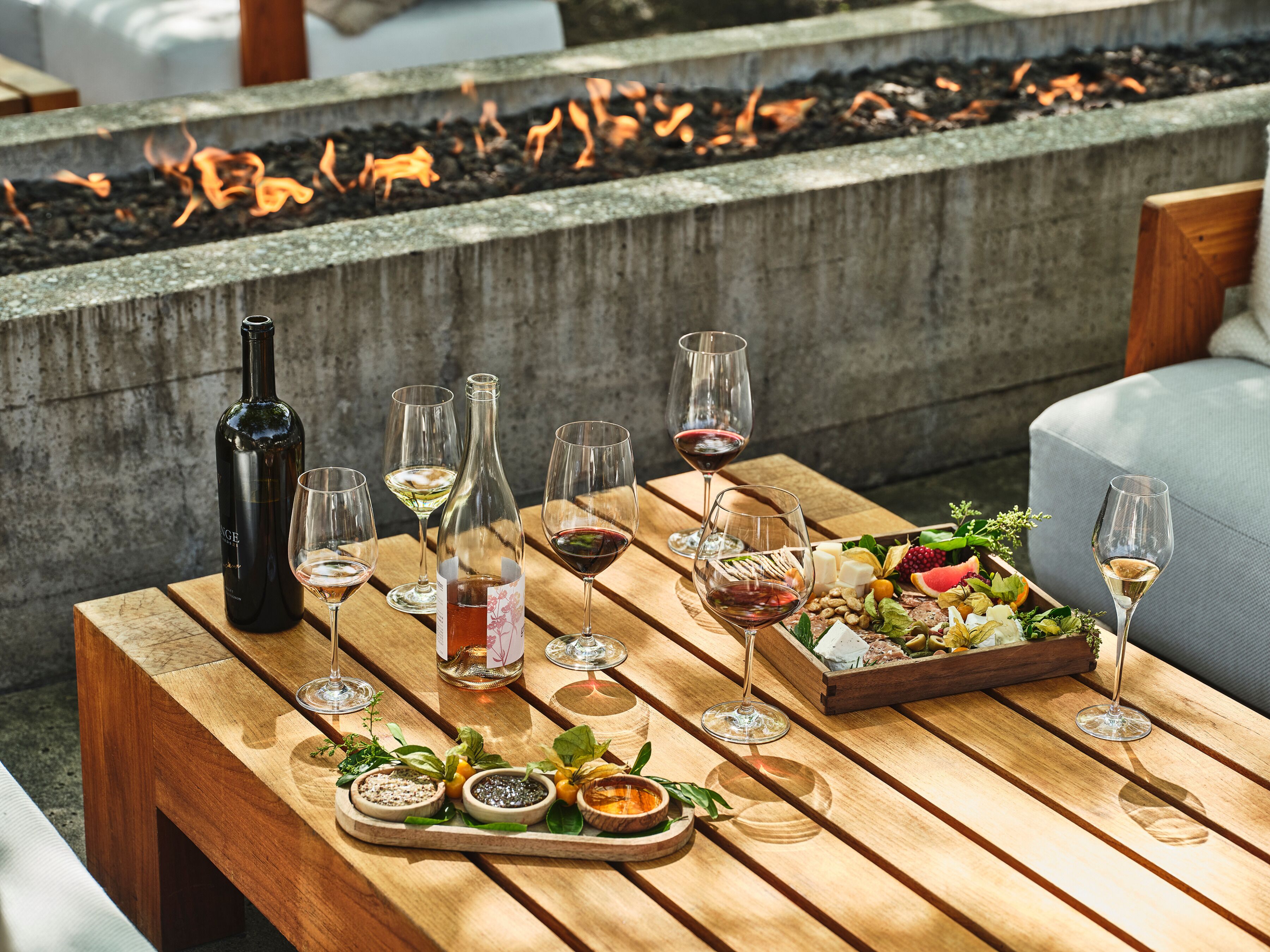 A wooden table set with wine glasses, bottles, and a charcuterie board.