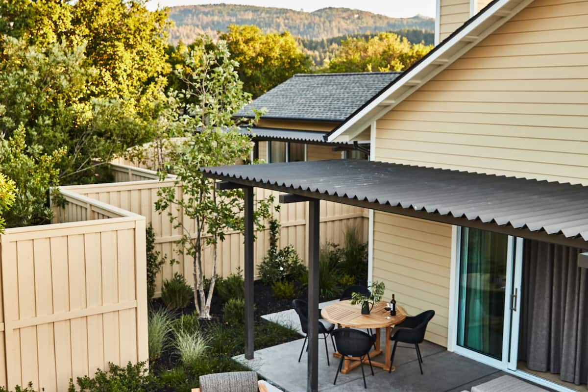 A patio with a table and chairs, surrounded by a wooden fence and greenery.