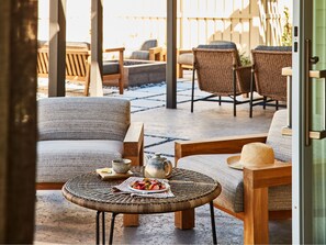 A cozy outdoor seating area with wicker furniture and a round table with a plate of food and a teapot.
