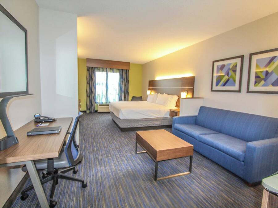 Quarto de hotel com cama, um sofá azul, uma escrivaninha com computador e uma mesinha.