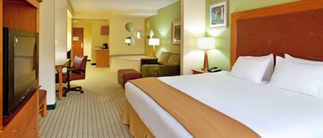 A hotel room with a large bed, a television, a desk with a chair, a sofa, and a small kitchenette.