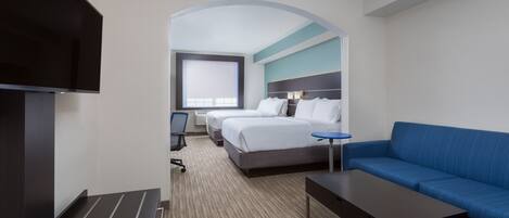 A hotel room with a TV, two beds, a sofa, a small table, and a chair.