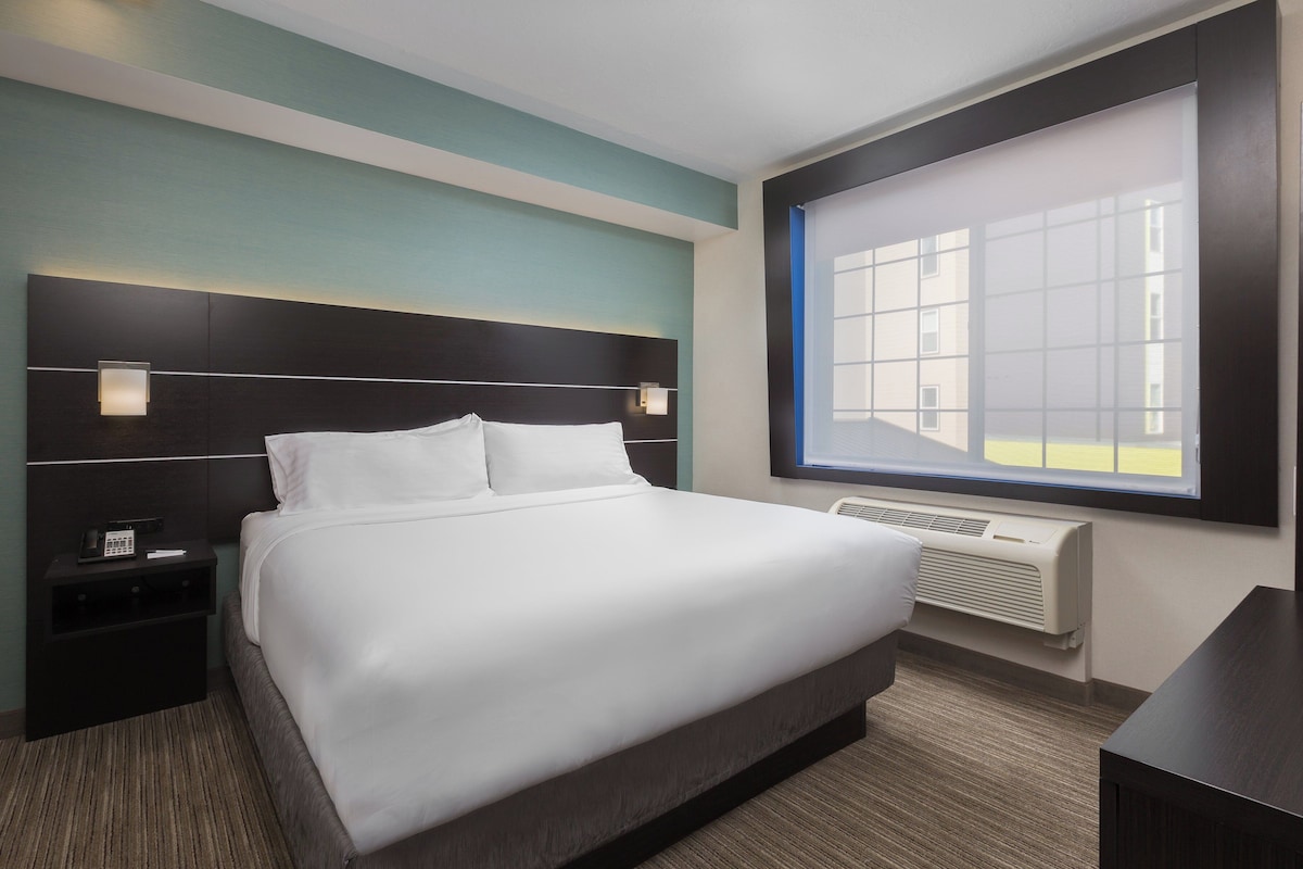 Habitación de hotel con una cama grande, mesitas de noche, ventana con vistas y aire acondicionado integrado.