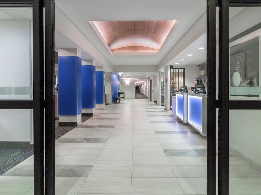 A hotel reception area with a long corridor leading to a reception desk, blue privacy booths, and a modern ceiling design.