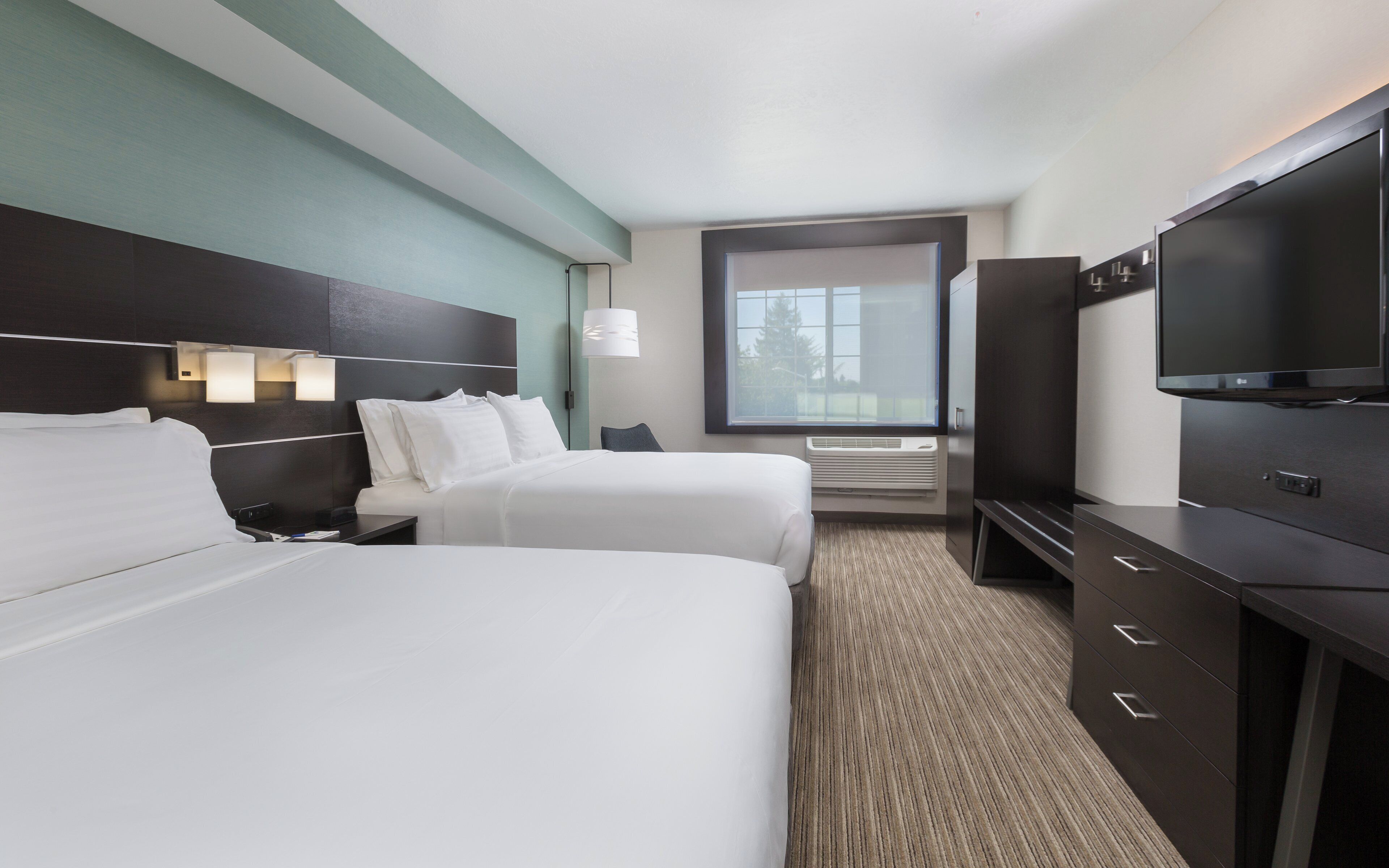 A hotel room with two beds, a TV, a desk, and a window.