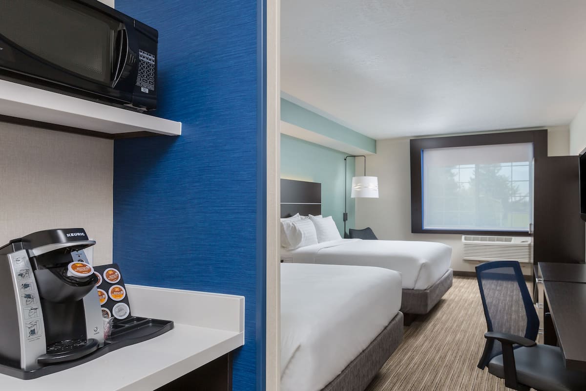 A hotel room with a kitchenette, two beds, a TV, and a window with a view.
