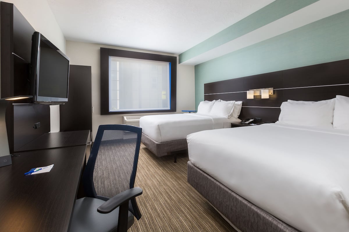 A hotel room with two beds, a desk, a chair, a TV, and a window with blinds.