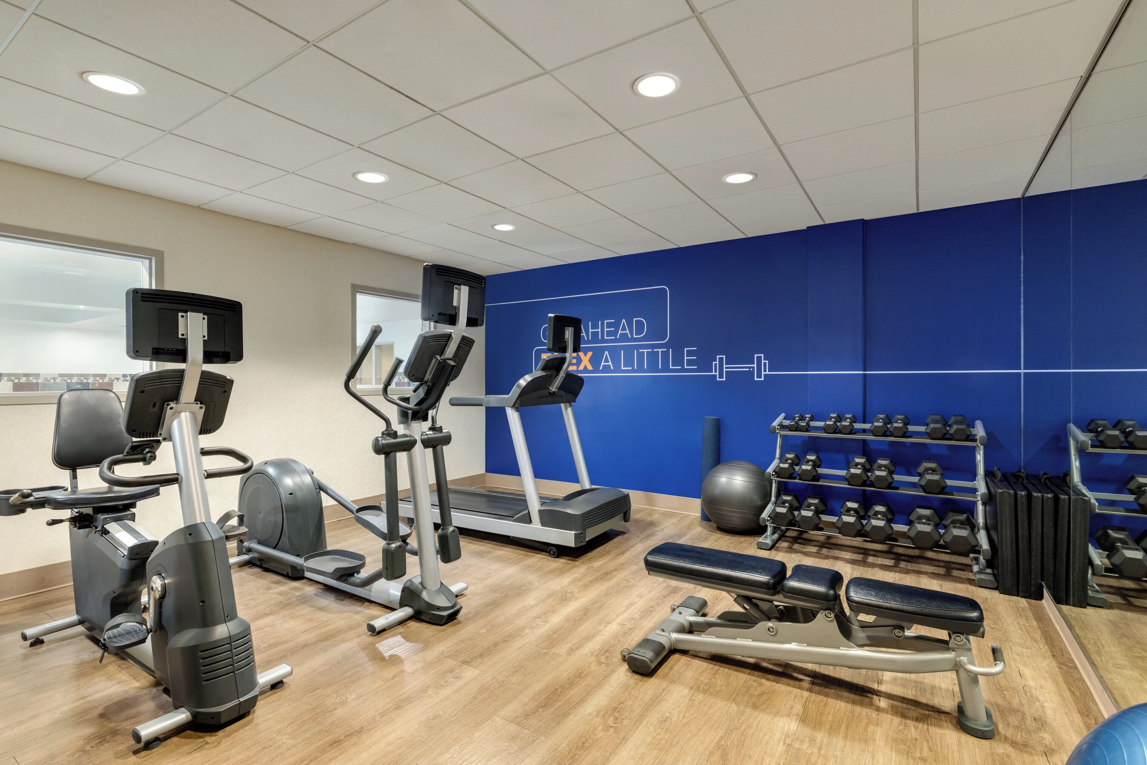 A gym with various exercise equipment, including treadmills, ellipticals, and dumbbells.