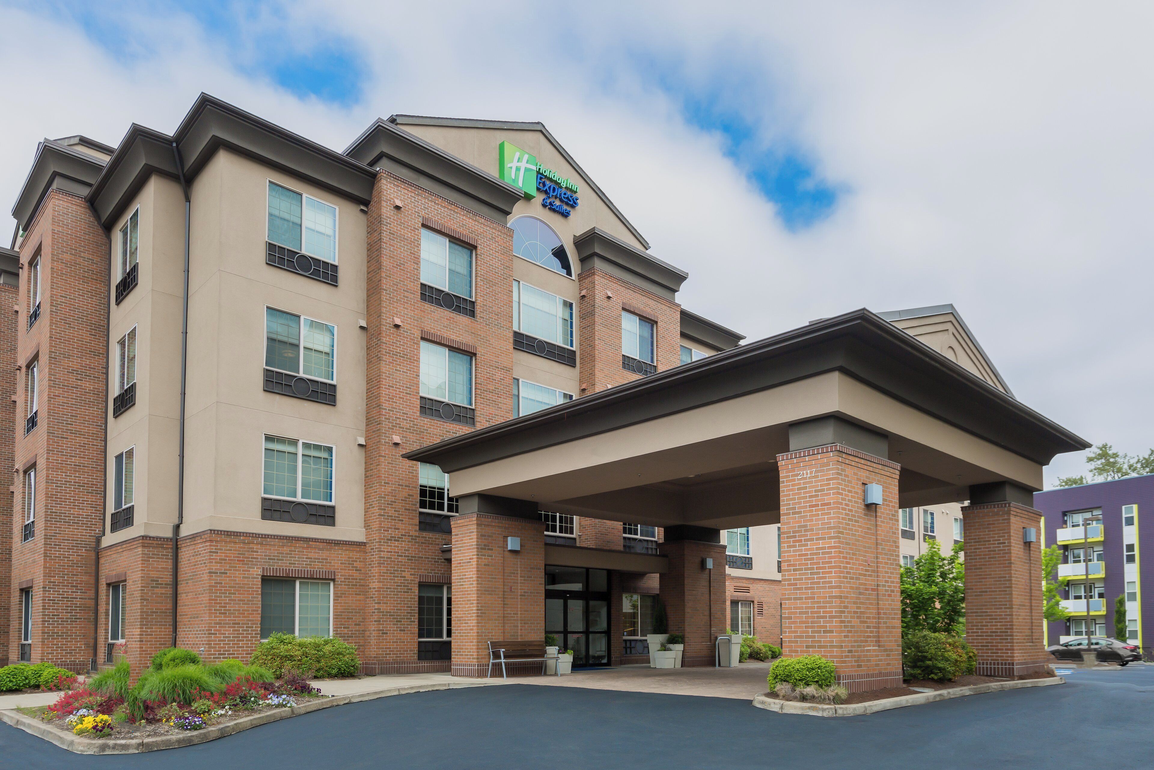 Un hôtel Holiday Inn Express & Suites avec une façade en briques, de nombreuses fenêtres et une entrée abritée.