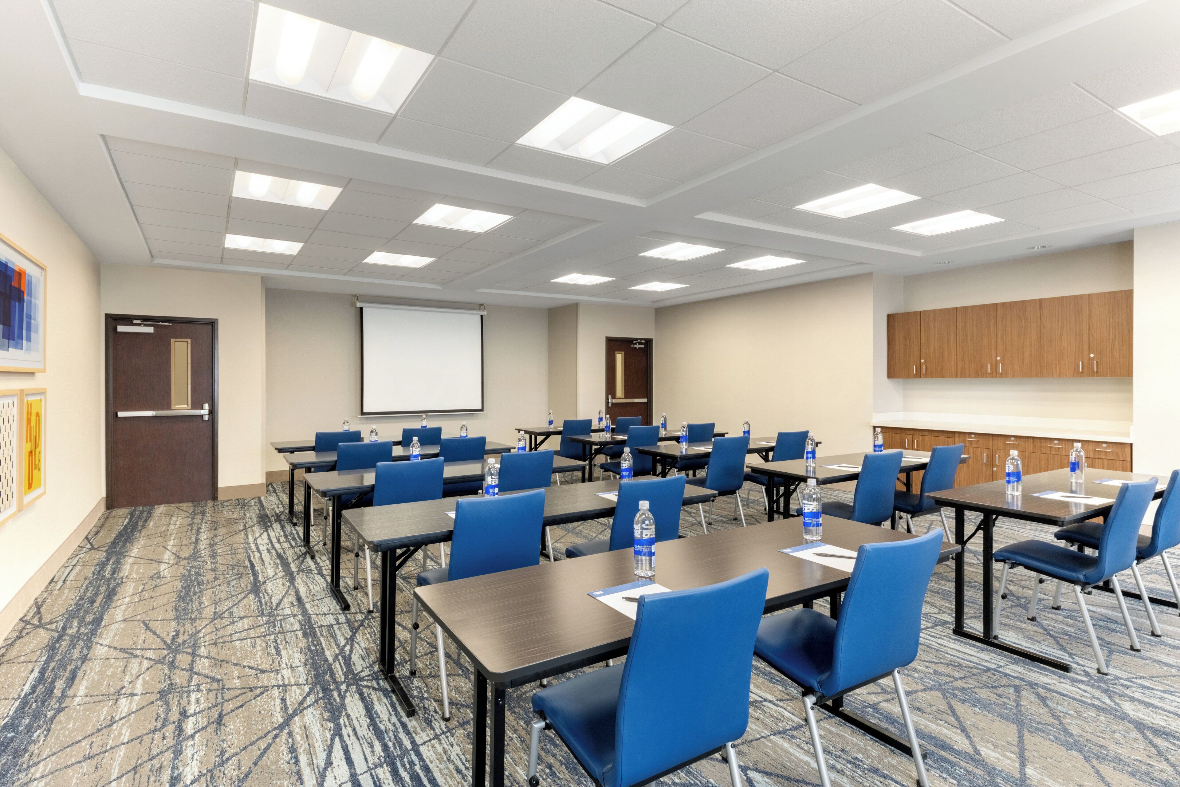 A conference room with tables, chairs, and a projector screen.