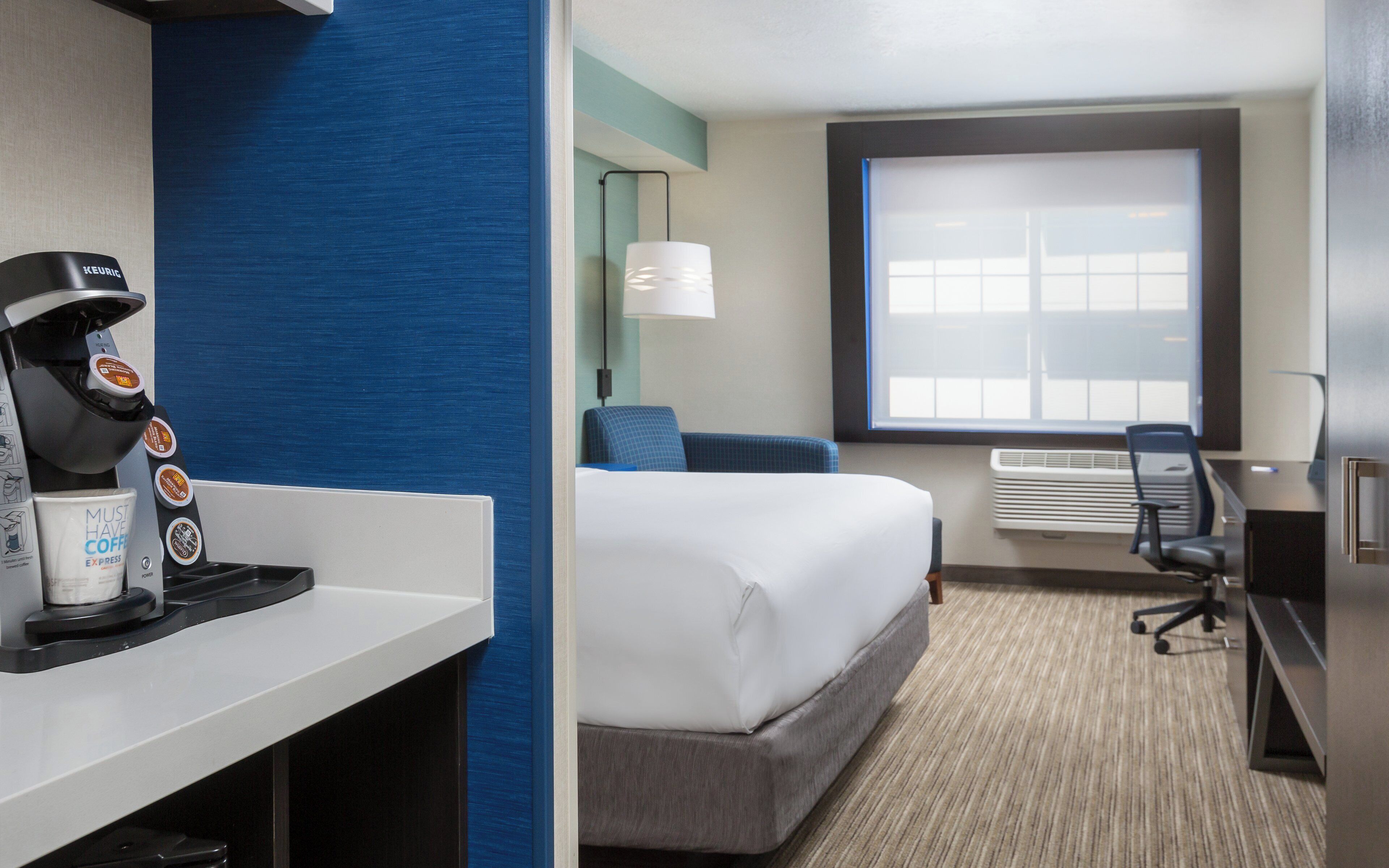 A hotel room with a bed, a desk, a coffee machine, and a window.