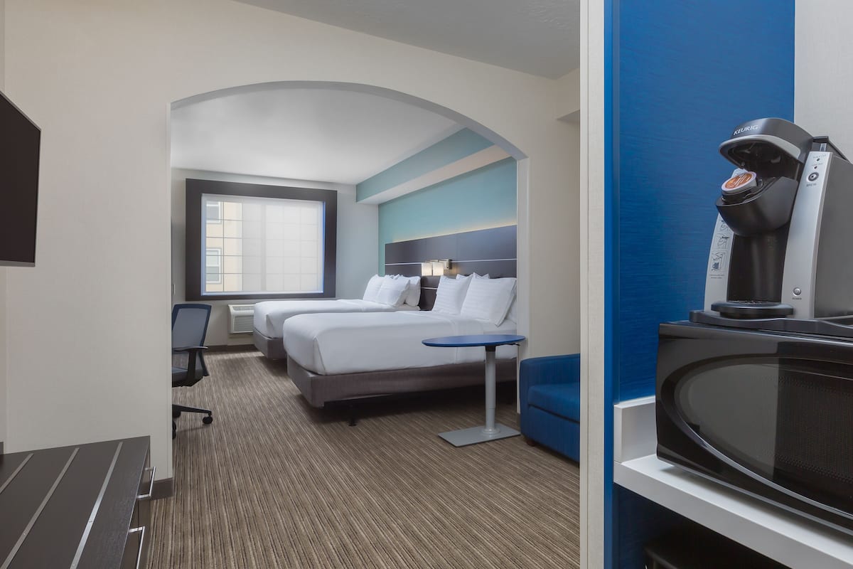 A hotel room with a bed, a desk, a chair, a coffee maker, and a television.