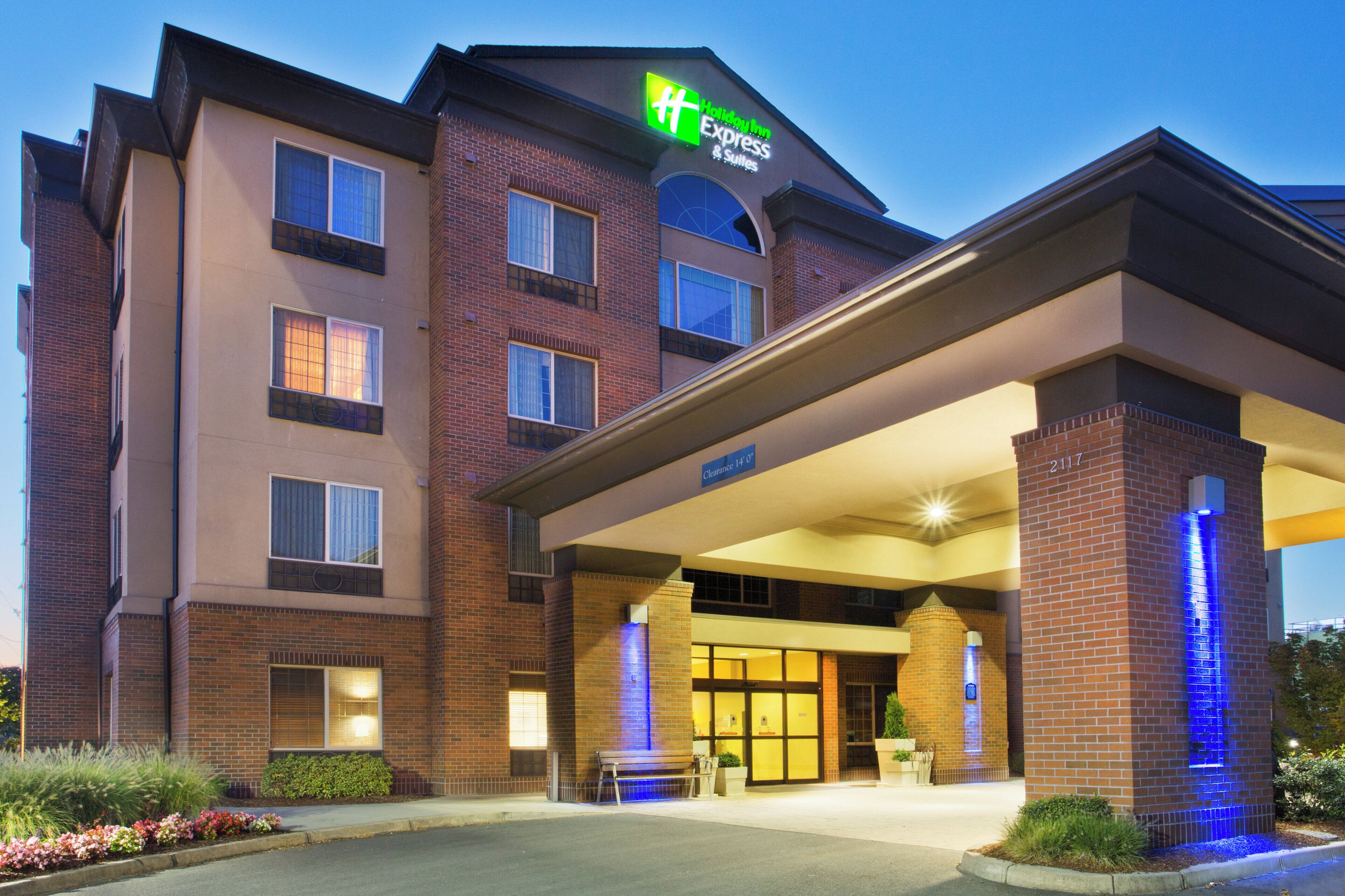 Un hotel Holiday Inn Express con fachada de ladrillo, un acceso cubierto y una fuente iluminada en azul.