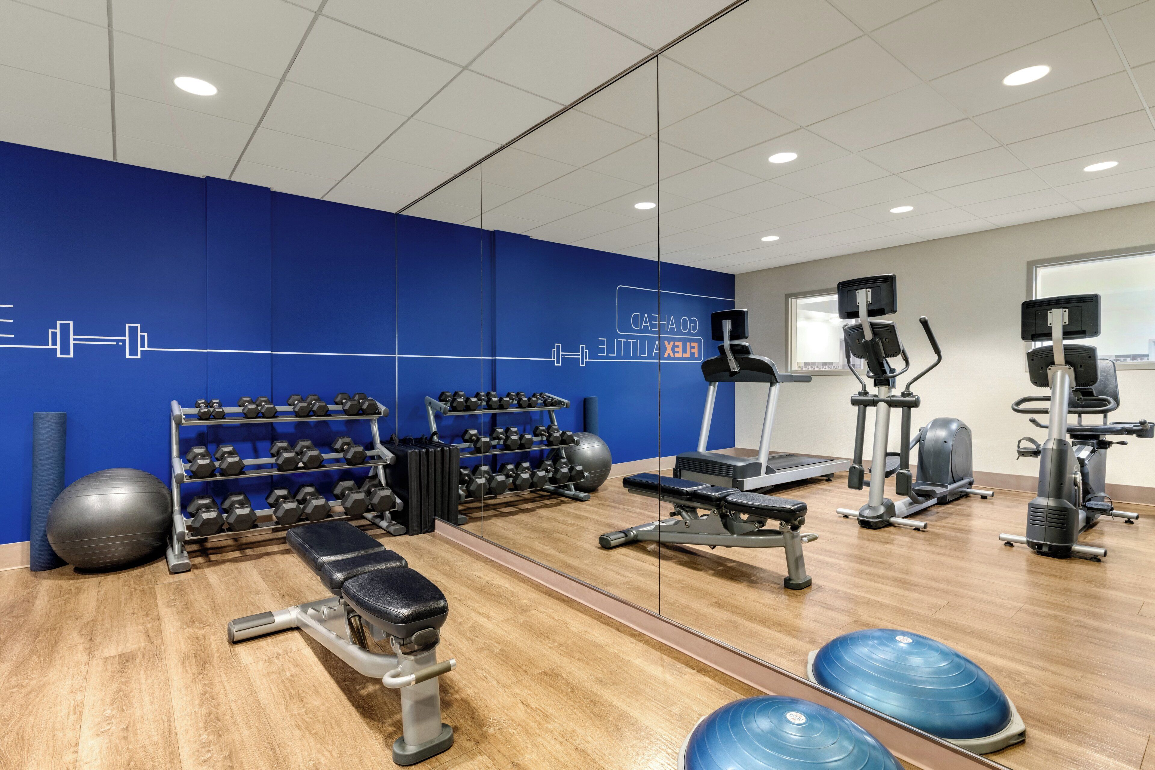 Uma academia com equipamentos de exercícios, um espelho e uma parede azul com frases motivacionais.