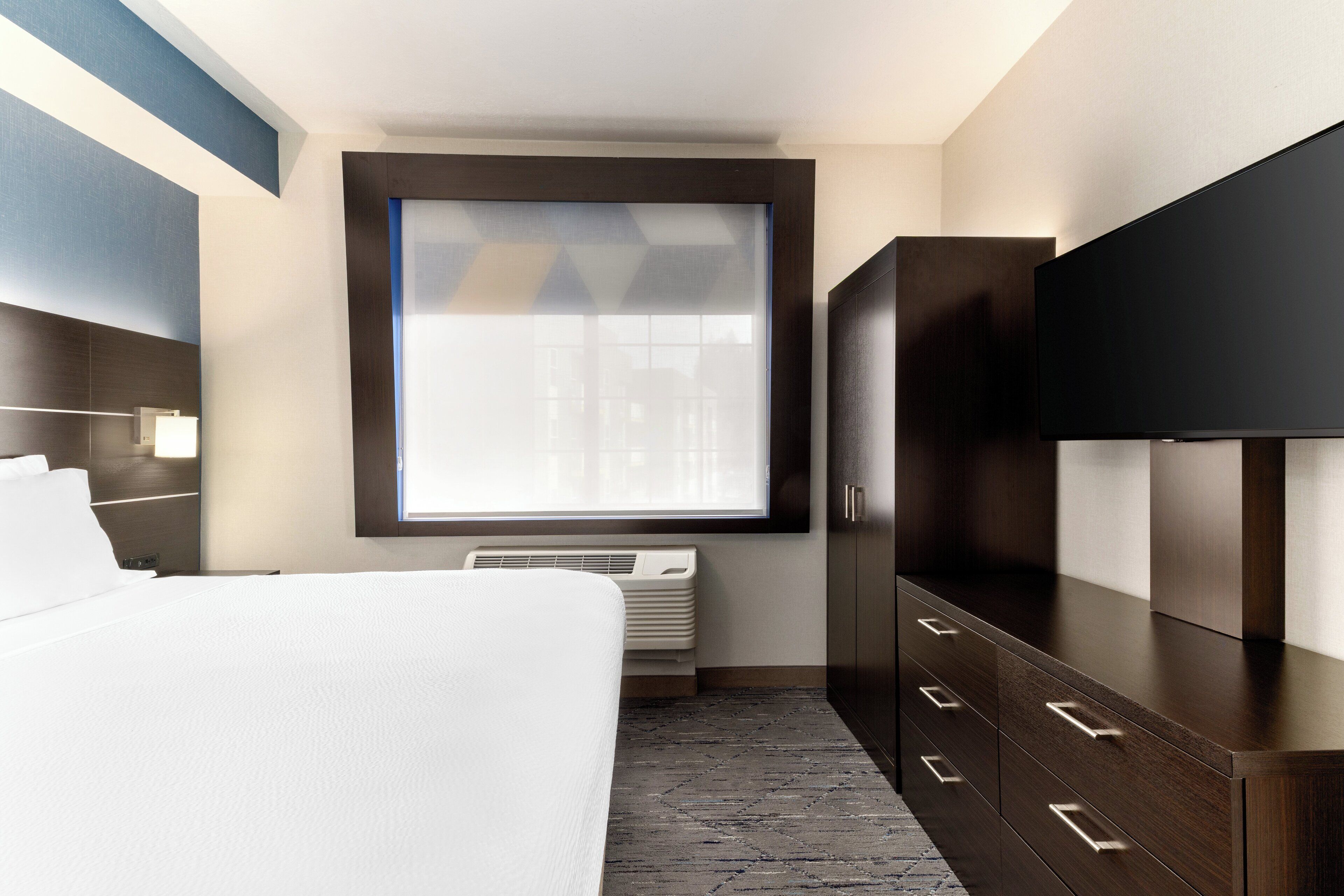 Une chambre d’hôtel équipée d’un lit, d’une télévision, d’une armoire et d’une fenêtre avec des stores.
