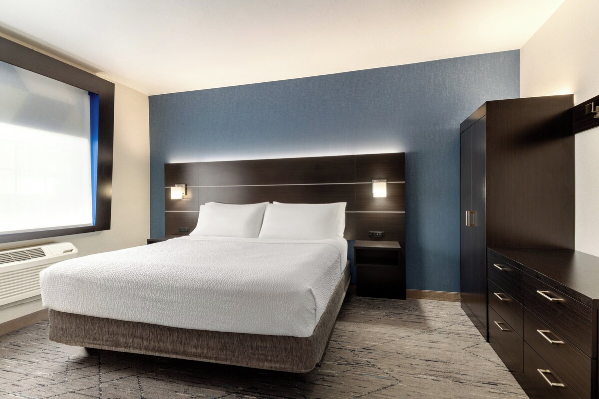 A modern hotel room with a large bed, bedside tables, a wardrobe, and a view of the outdoors.
