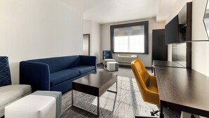 A modern hotel room with a blue sofa, a small white ottoman, a dark wooden table, a yellow chair, and a large window providing natural light. - Holiday Inn Express Hotel & Suites Eugene Downtown-University by IHG (Eugene)