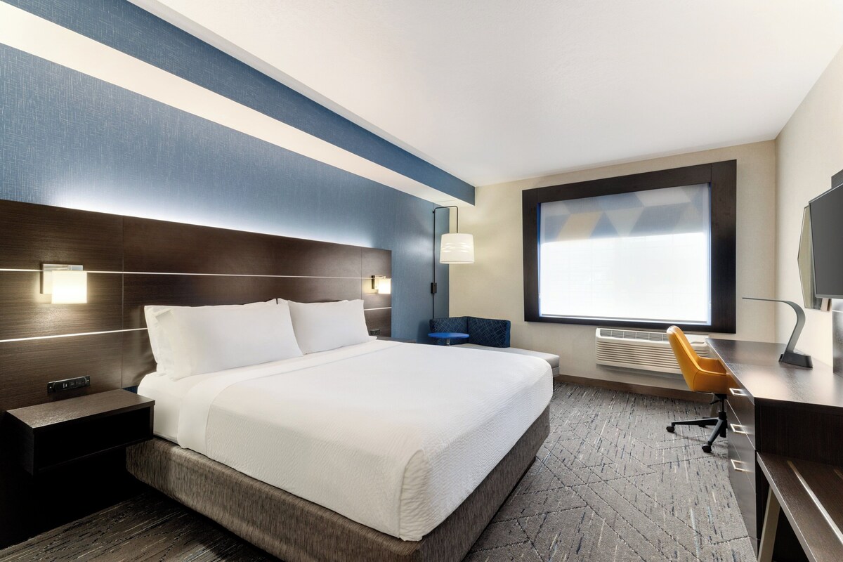 A hotel room with a bed, desk, chair, and a large window.