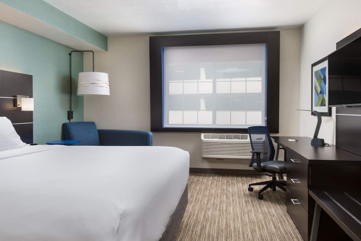 A hotel room with a bed, a desk with a chair, a TV, and a window with blinds.