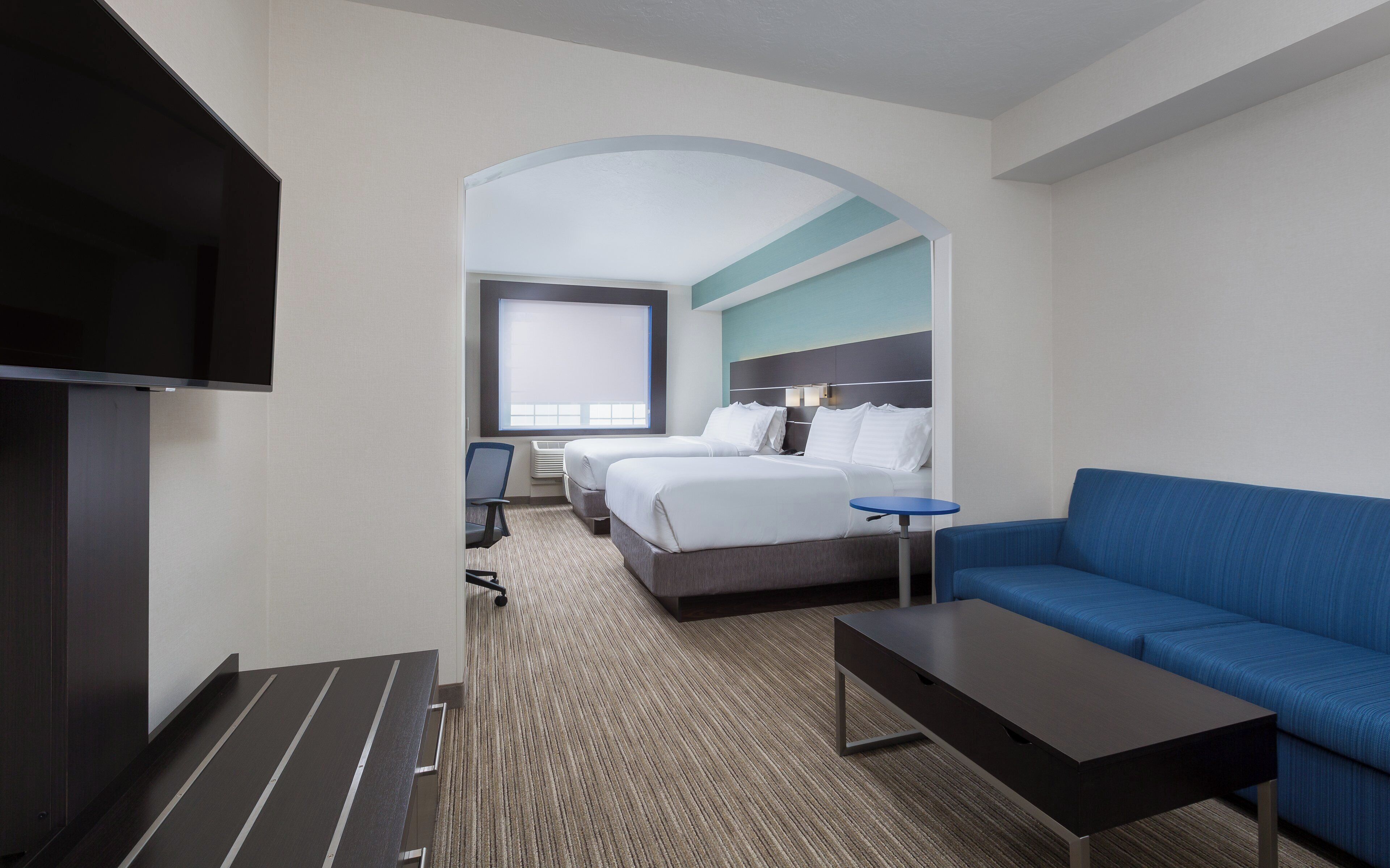A hotel room with a TV, two beds, a sofa, a small table, and a window.