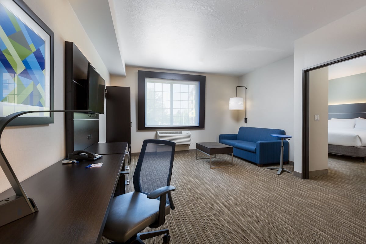 A hotel room with a desk, chair, blue sofa, and a bed.