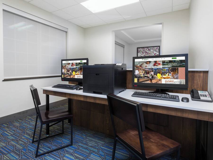 Une chambre d’hôtel équipée d’un bureau, de deux écrans, d’un clavier, d’une souris, d’un téléphone et d’une chaise.
