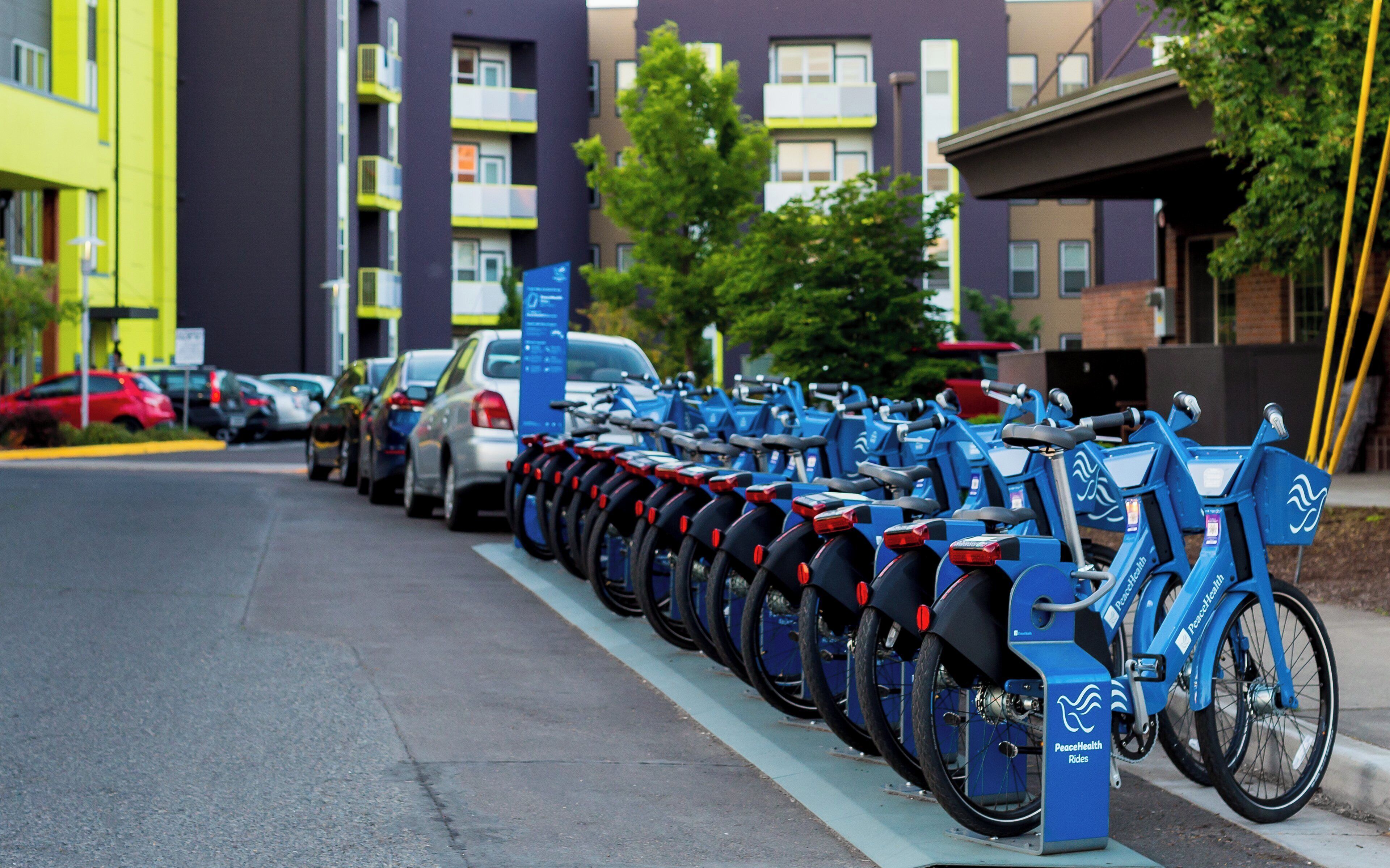 Een rij blauwe fietsen geparkeerd langs een trottoir, met een gebouw op de achtergrond.