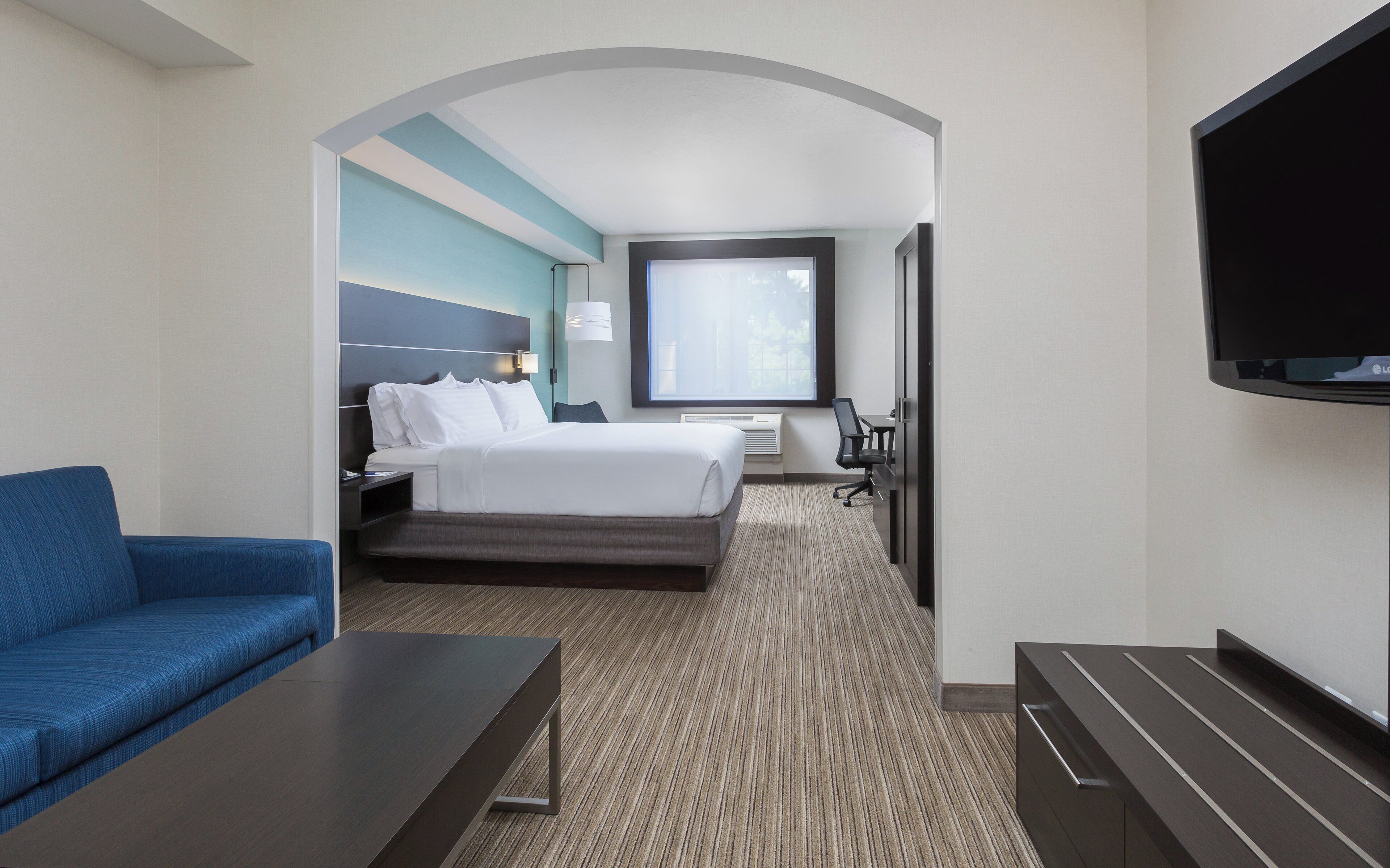 A hotel room with a bed, a desk, a chair, a TV, and a sofa.