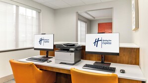 A hotel reception desk with two computer monitors displaying the Holiday Inn Express logo, a printer, and two orange chairs. - Holiday Inn Express Hotel & Suites Eugene Downtown-University by IHG (Eugene)