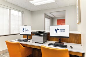 Un mostrador de recepción de hotel con dos monitores de computadora que muestran el logotipo de Holiday Inn Express, una impresora y dos sillas naranjas.