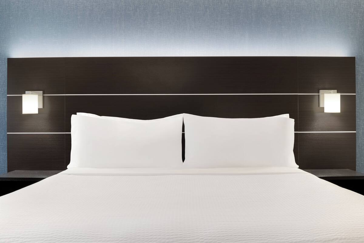 A modern hotel room with a large bed, two bedside lamps, and a dark headboard.