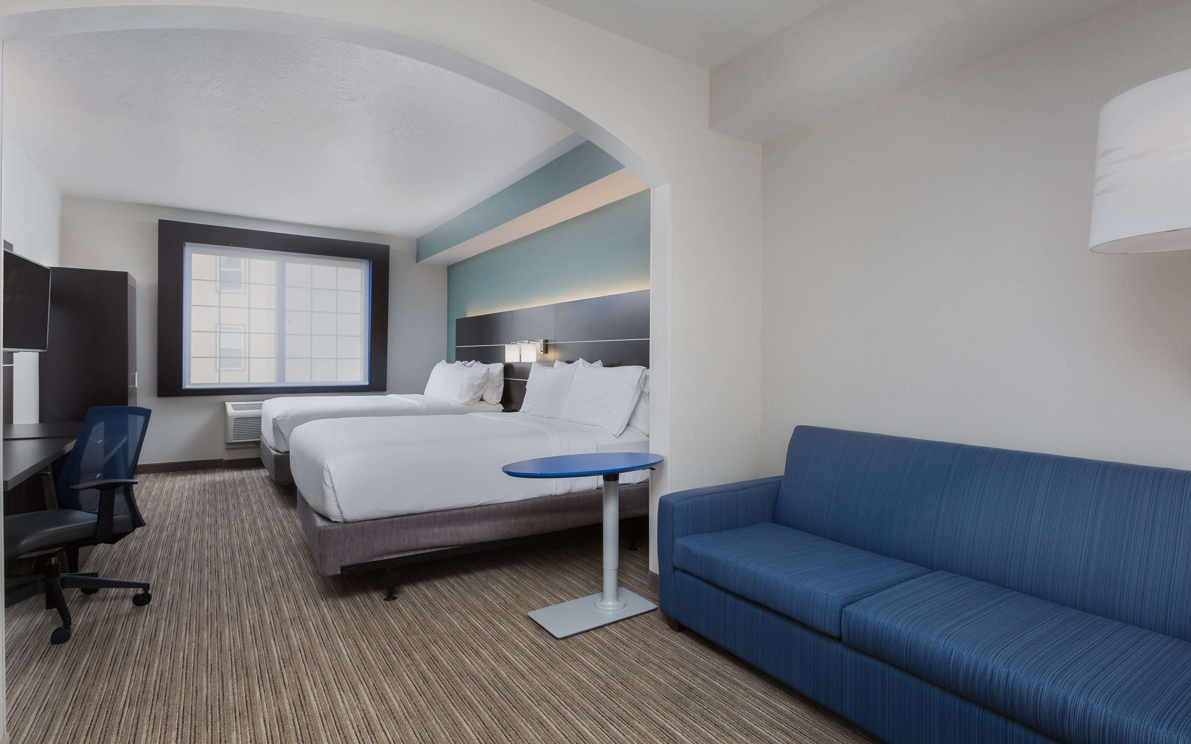 Una habitación de hotel con una cama, un escritorio, una silla, un sofá azul y una pequeña mesa.