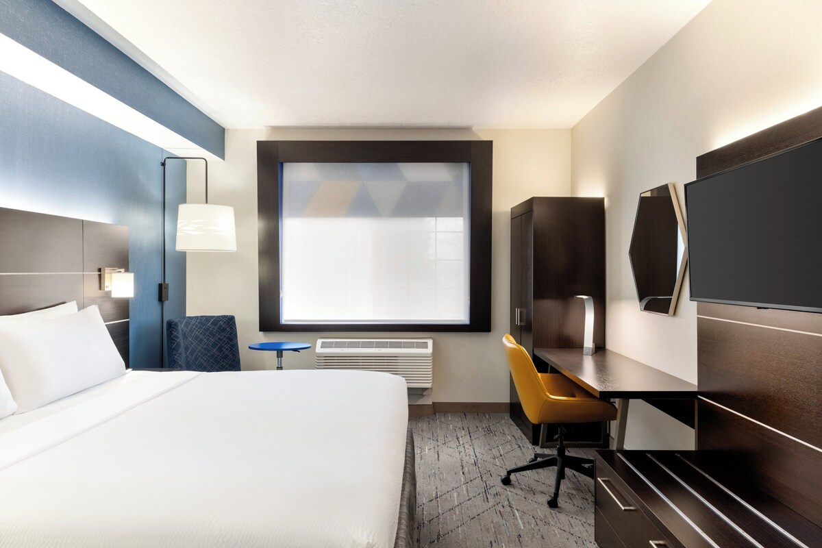 A hotel room with a bed, desk, chair, TV, and a large window.