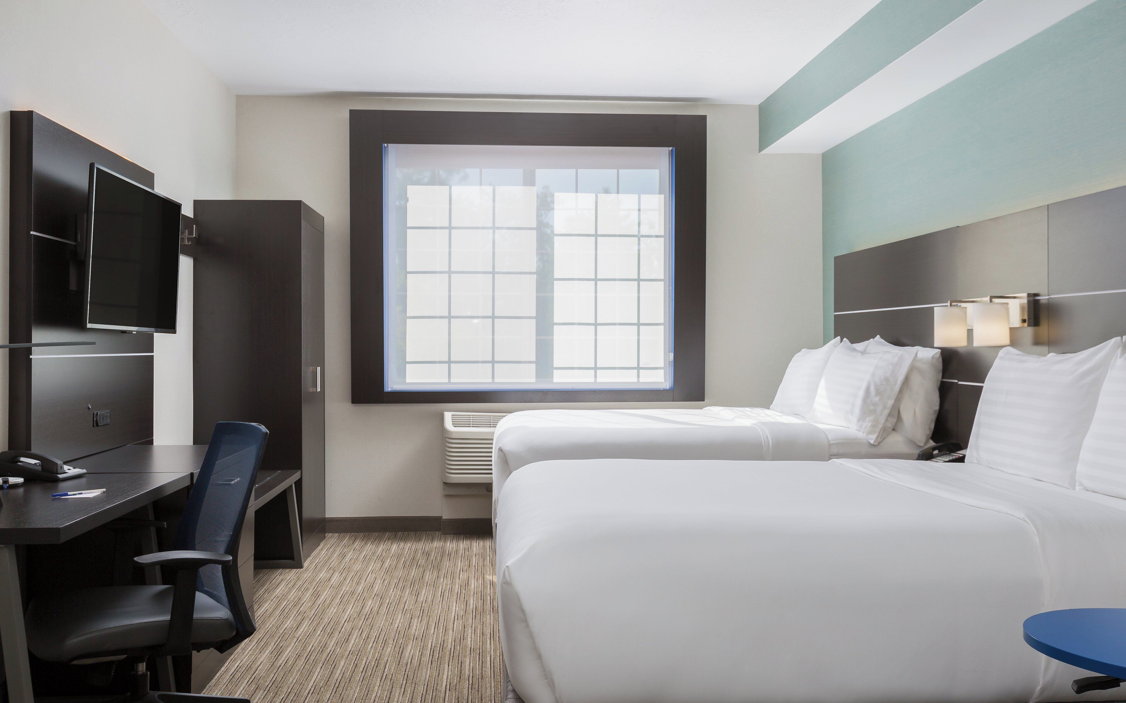 Een hotelkamer met een bed, een bureau met stoel, een televisie en een raam.