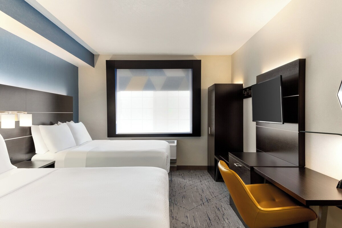 A hotel room with two beds, a desk, a chair, a television, and a large window.