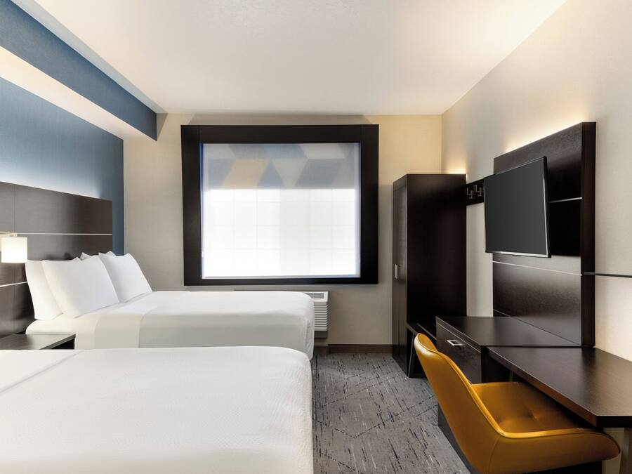 A hotel room with two beds, a desk, a chair, a television, and a large window.
