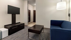 A modern living room with a flat-screen TV, dark wooden furniture, a blue sofa, and a floor lamp. - Holiday Inn Express Hotel & Suites Eugene Downtown-University by IHG (Eugene)