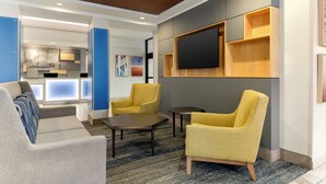 A modern lobby with a sofa, two yellow armchairs, a coffee table, and a flat-screen TV mounted on a wooden shelf. - Holiday Inn Express Hotel & Suites Eugene Downtown-University by IHG (Eugene)