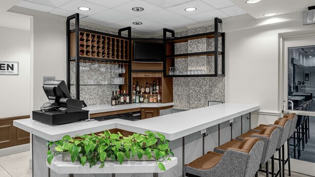 Eine moderne Bar mit einer weißen Theke, Barhocker, einem Weinkühlschrank und einem Fernseher.