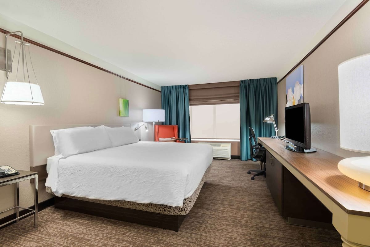 A hotel room with a bed, desk, chair, TV, lamp, and a window with curtains.