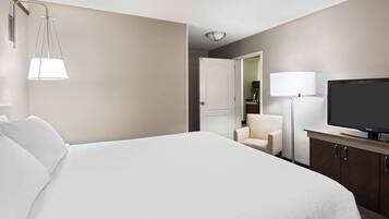 A hotel room with a large bed, a TV, a chair, and a desk with a lamp.