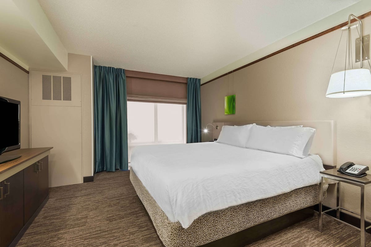 A hotel room with a large bed, a desk with a telephone, a television, and a window with curtains.