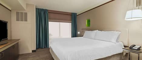 Habitación de hotel con una cama grande, un escritorio con teléfono, televisión y ventana con cortinas.