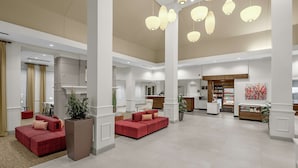 Eine großzügige Lobby mit roten Sofas, einem Empfangstresen und hängenden Pendelleuchten.