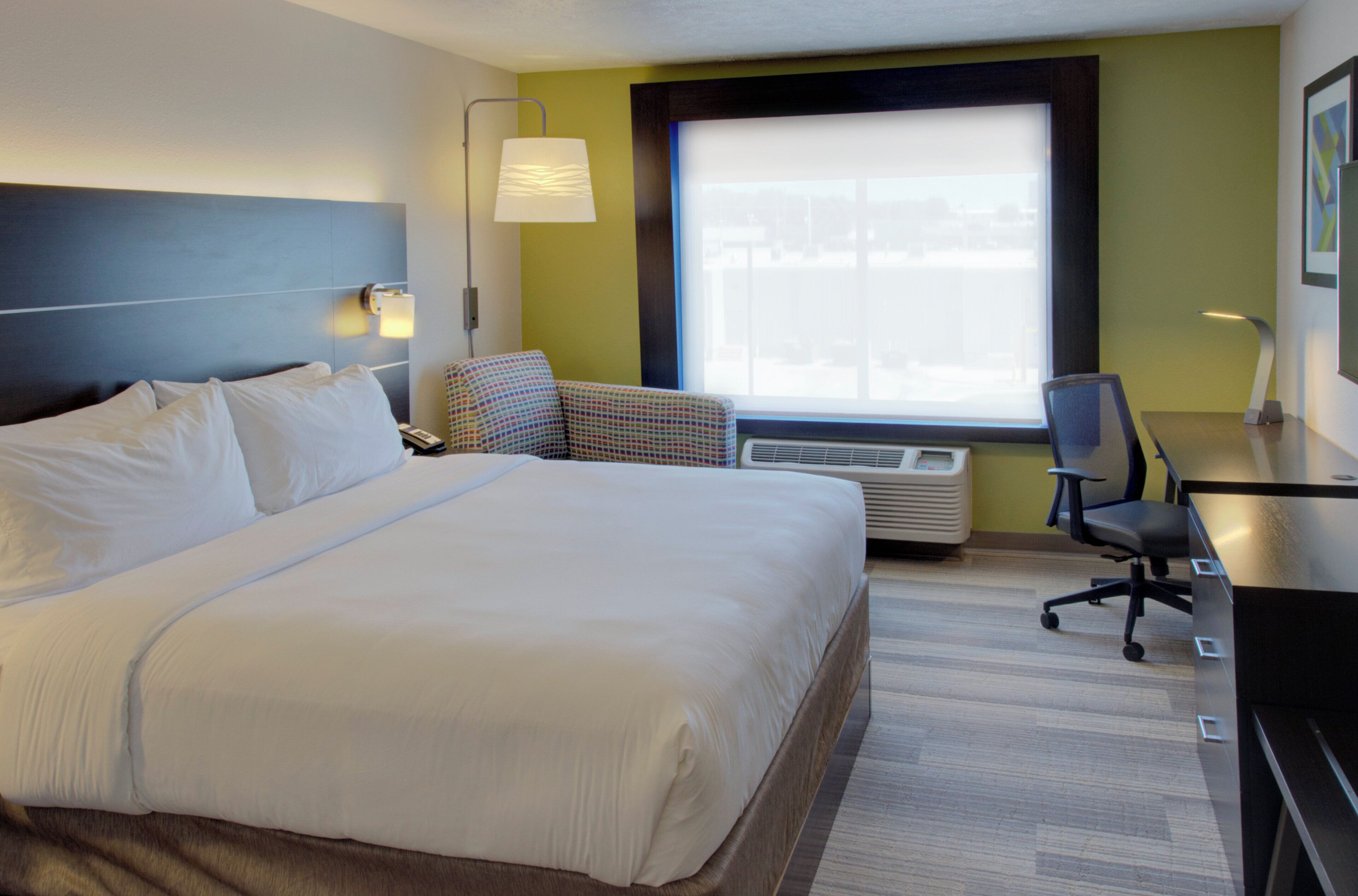 Une chambre d’hôtel avec un grand lit, un bureau, une chaise, une fenêtre donnant sur un beau paysage et un climatiseur fixé au mur.