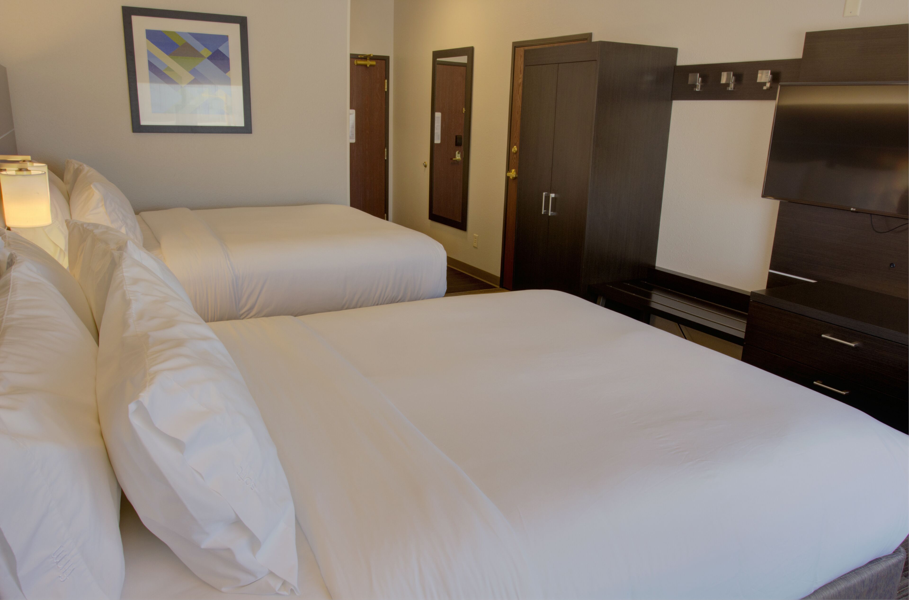 Habitación de hotel con dos camas individuales, un armario, un espejo y un televisor.