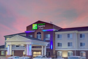 Edificio de Holiday Inn Express con un letrero llamativo, acceso cubierto y estacionamiento con varios autos.