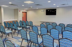 A conference room with rows of blue patterned chairs, a white table, and a flat-screen TV mounted on the wall. - Holiday Inn Express Hotel & Suites Le Mars by IHG (Le Mars)