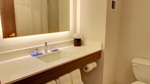 Un baño con lavamanos blanco, espejo, toalla y retrete.