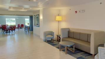 A hotel lobby with a reception desk, a sofa, chairs, and a dining area with tables and chairs.